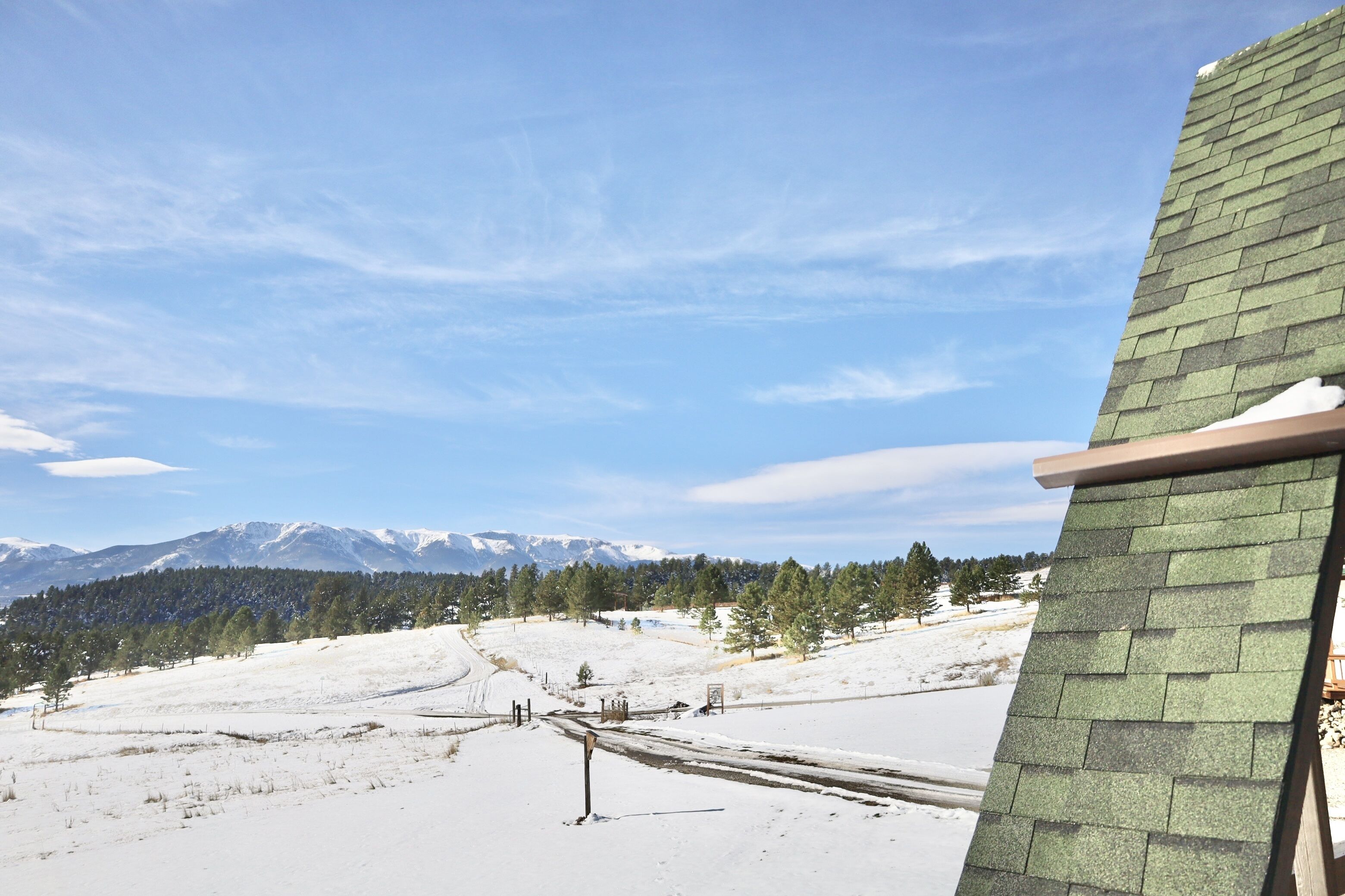 A snowy landscape with a clear sky, a mountain range in the background, and a building with a green roof.