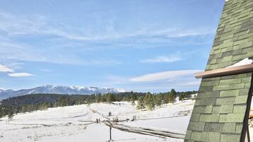 A snowy landscape with a clear sky, a mountain range in the background, and a building with a green roof.