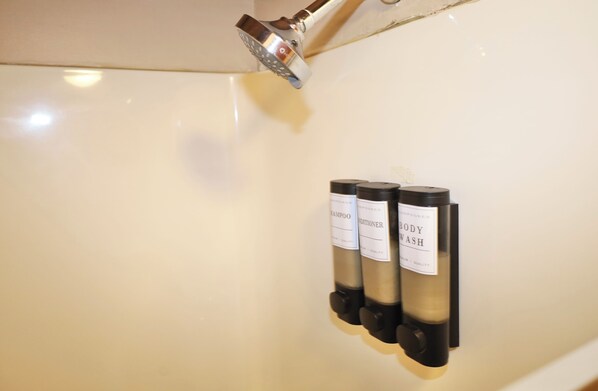 A wall-mounted showerhead and three bottles of body wash.