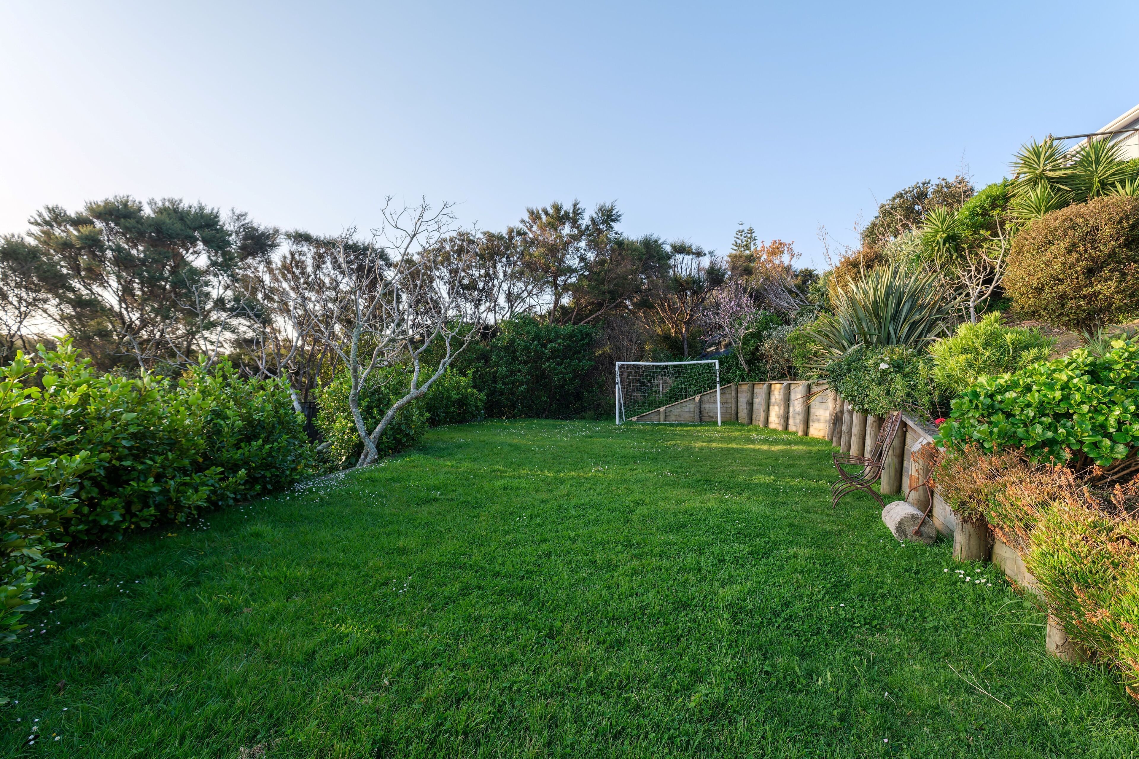 A well-maintained grassy area with a soccer goal, surrounded by dense shrubbery and trees.