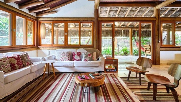 A spacious living area with a white sofa, wooden coffee table, and a view of the outdoors. - Praia de Itamambuca - Bali House (Ubatuba)