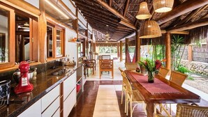 A kitchen with a red mixer, a dining area with wicker chairs, and a thatched roof. - Praia de Itamambuca - Bali House (Ubatuba)