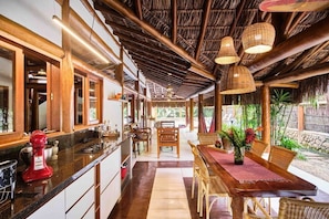 A kitchen with a red mixer, a dining area with wicker chairs, and a thatched roof.