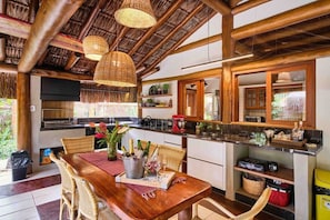 A rustic kitchen with wooden beams, a dining area with wicker chairs, and a table set with wine glasses and bottles.