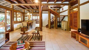 A spacious living area with a wooden ceiling, a TV stand, and a staircase. - Praia de Itamambuca - Bali House (Ubatuba)