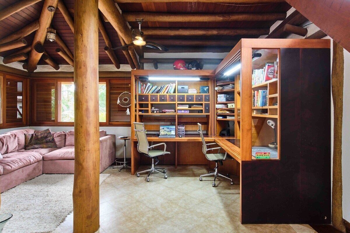 Une pièce chaleureuse avec un plafond en bois, un canapé rose, un bureau avec deux chaises et une grande bibliothèque.