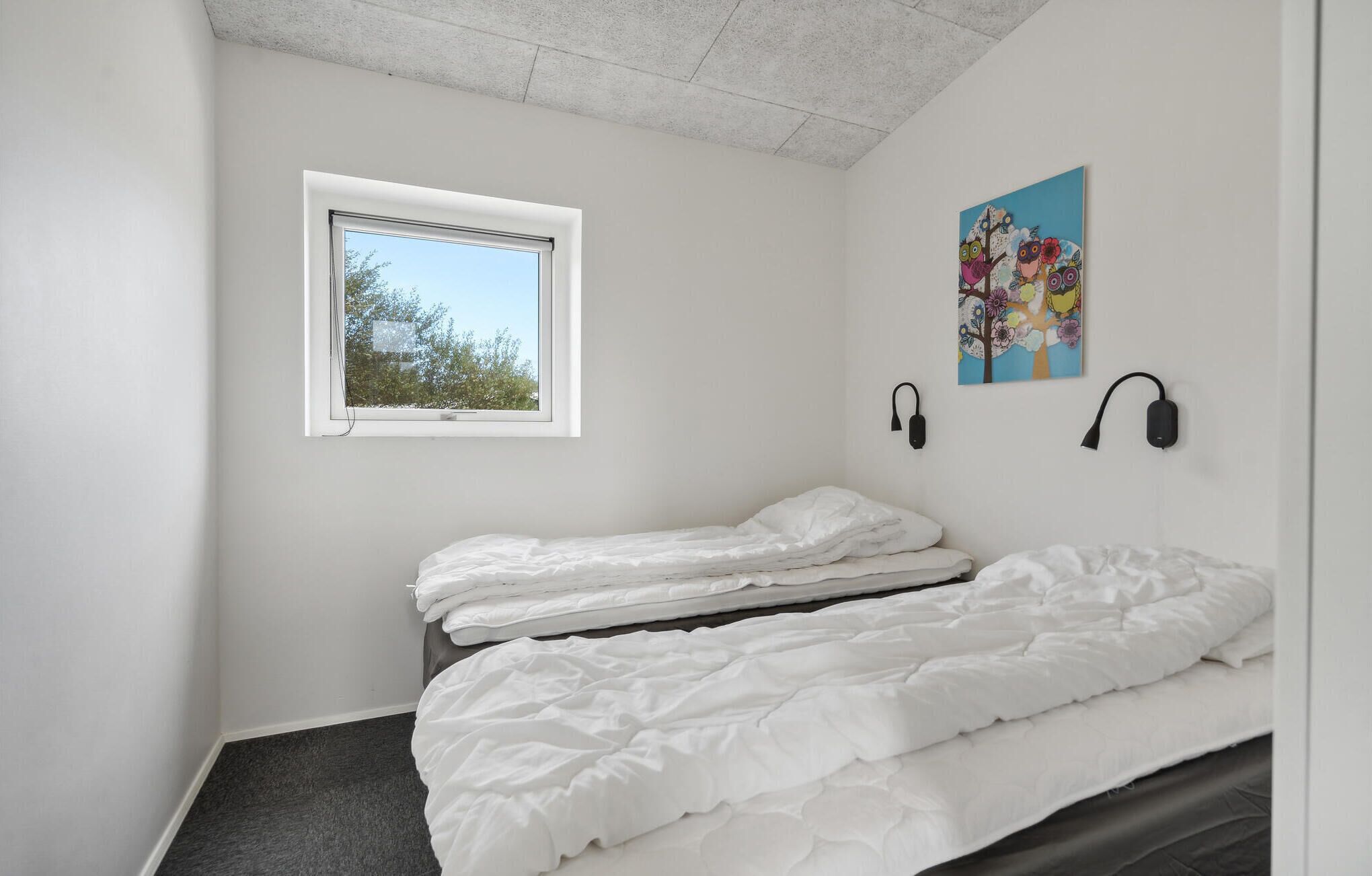 Et soveværelse med to senge, et vindue og en lampe monteret på væggen.