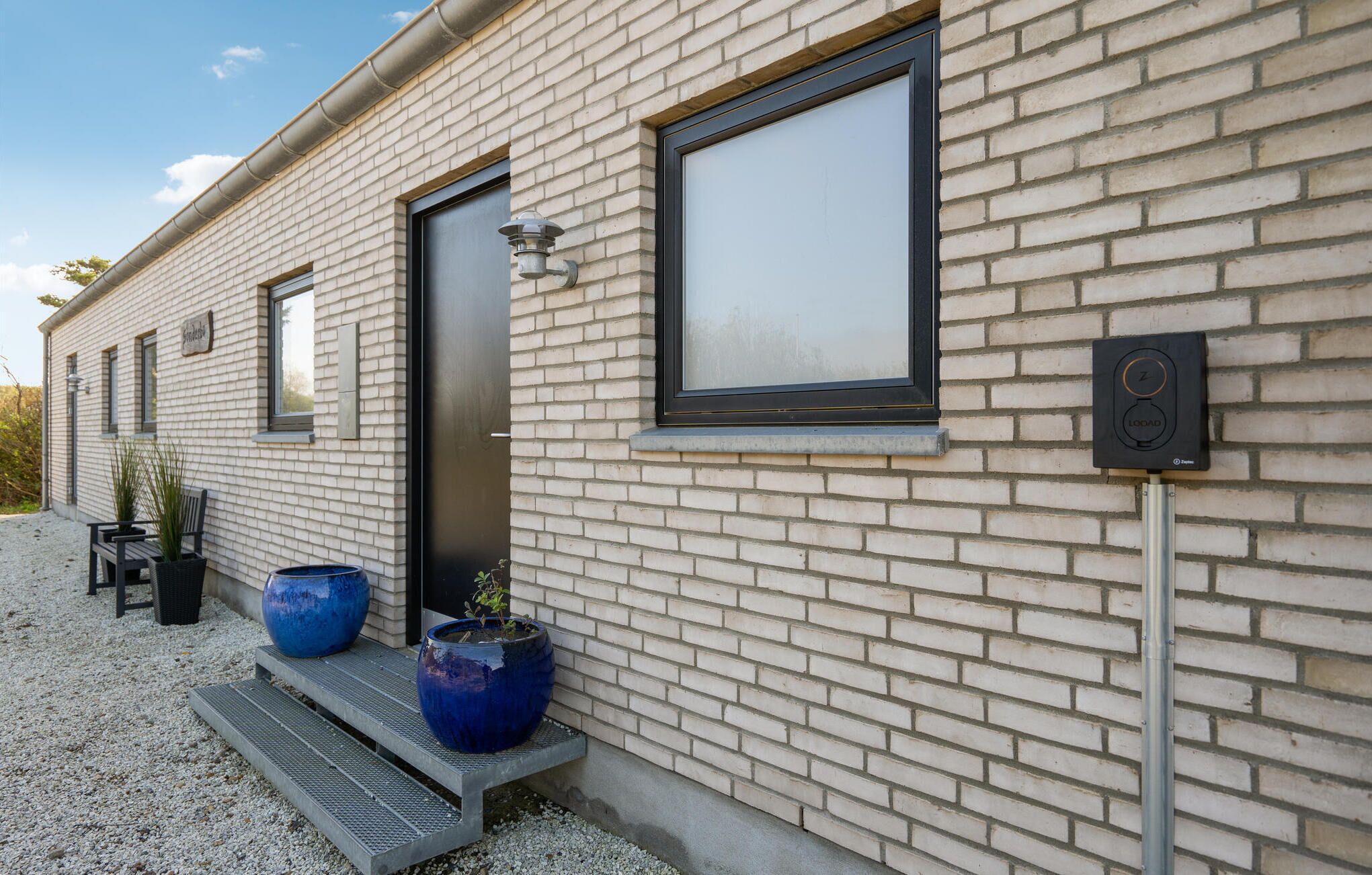 Il s’agit d’un bâtiment moderne avec une façade en briques, une grande fenêtre et une porte. On y trouve deux grands bacs à fleurs bleus au niveau du sol.
