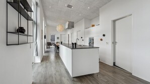 Et moderne køkken med en central ø, hvide skabe og et spiseområde med et bord og stole.
