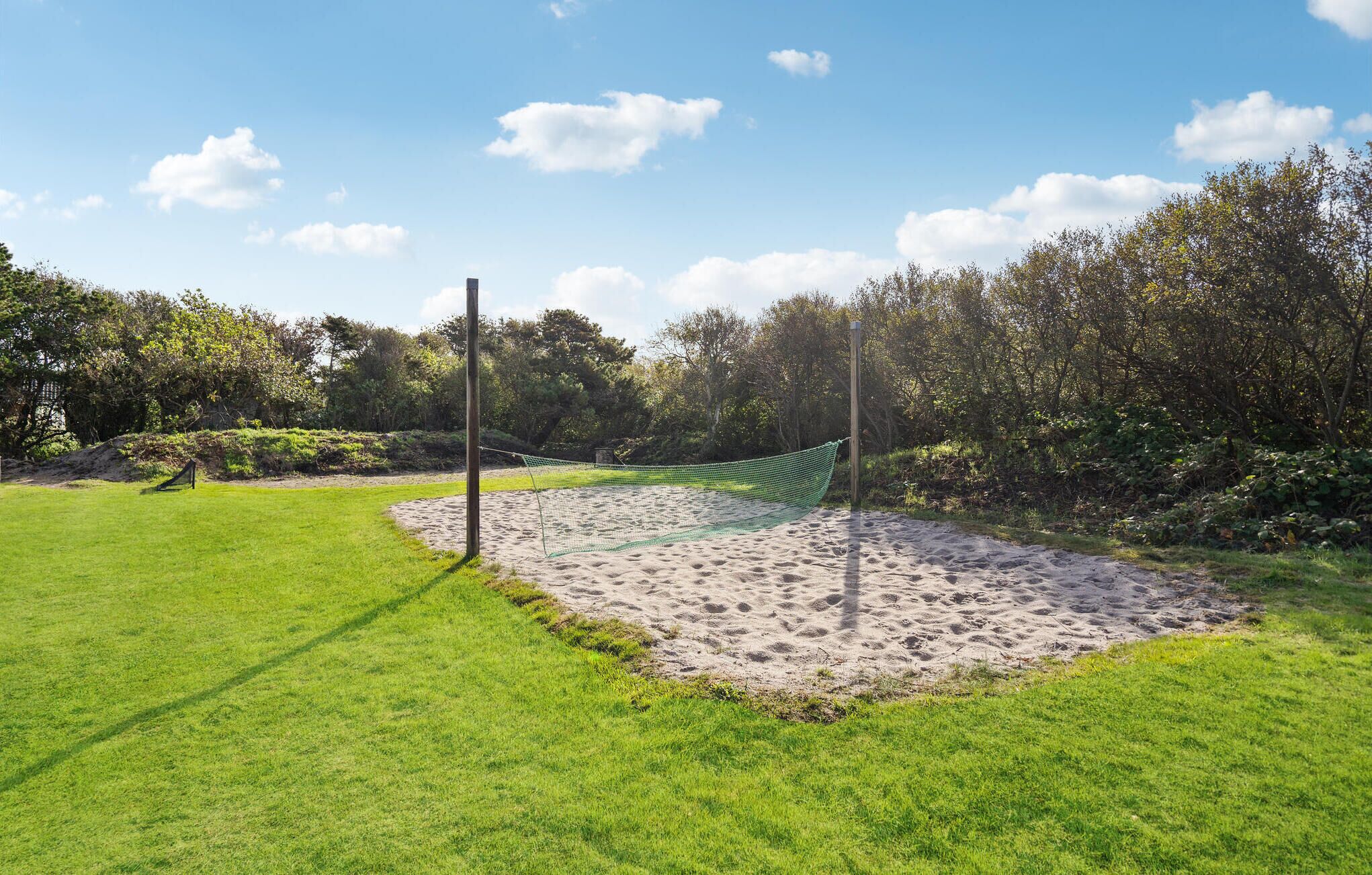 Un terrain de volley-ball avec un filet, entouré d’herbe verte et d’arbres.