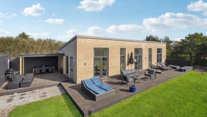 Et moderne hus med terrasse, udendørs møbler og grill.