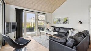 A modern living room with a black leather sofa, a black chair, a white coffee table, and a TV. - Stunning home in Broager with WiFi (Broager)