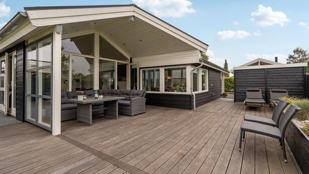 A covered outdoor area with a wooden deck, a seating area with a table and chairs, and a glass-enclosed section with windows. - Stunning home in Broager with WiFi (Broager)