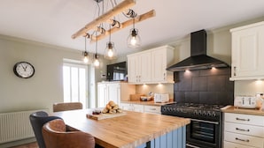 A kitchen with a wooden island, black stove, white cabinets, and pendant lighting. - Shieldhill Farm House (Falkirk)