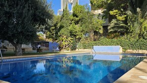 A swimming pool with a tiled edge, surrounded by trees and a building in the background.