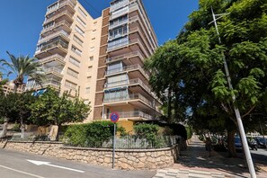 A multi-story residential building with balconies, a stone wall, and a pedestrian pathway.