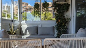 A sunlit room with wicker furniture, a cushioned bench, and hanging plants.
