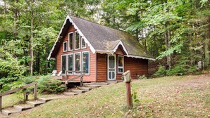 A cabin with a porch, wooden steps, and a forested backdrop. - Lakefront Ogema Vacation Rental Cabin w/ Fire Pit! (Ogema)