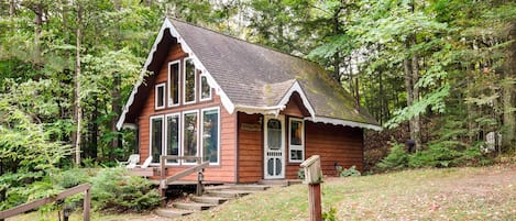 A cabin with a porch, wooden steps, and a forested backdrop.