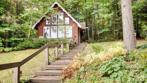 A wooden cabin with a staircase leading up to it, surrounded by a forest. - Lakefront Ogema Vacation Rental Cabin w/ Fire Pit! (Ogema)