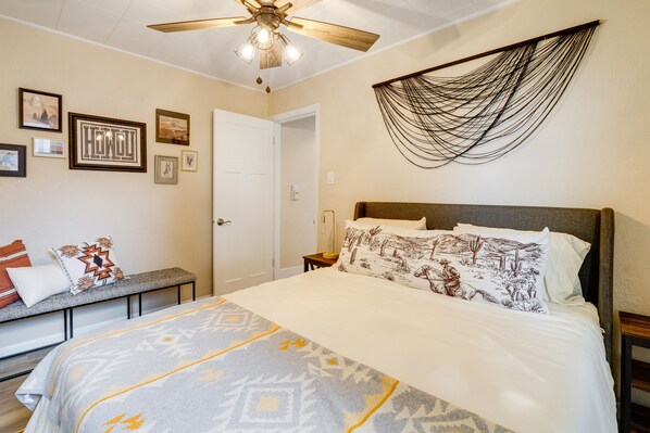 Un dormitorio con cama, un banco con almohadones, ventilador de techo y decoración en la pared.