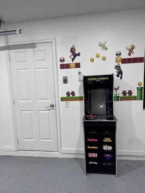 A room with a white door, a gaming console with various game titles, and wall decorations including characters and question marks.