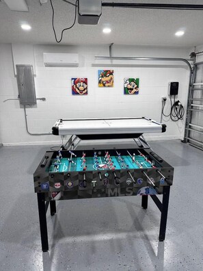 A foosball table in a room with white walls, a door, and three framed pictures of Mario.