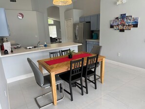 A modern kitchen with a central island, a dining area with a wooden table and chairs, and a refrigerator.