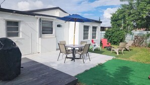 En uteplats med ett bord och stolar, en grill och ett blått parasoll.
