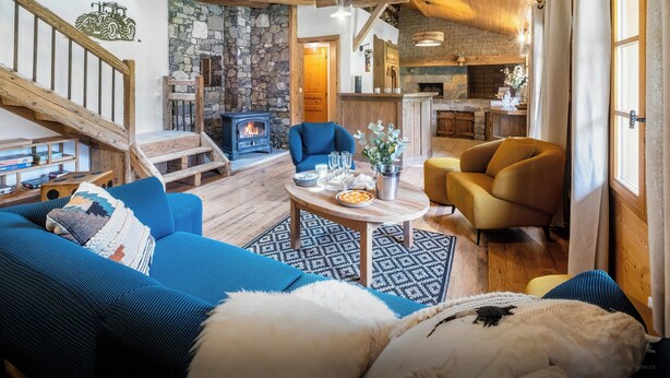 Un salon chaleureux avec une cheminée en pierre, un escalier en bois et un coin repas avec une table mise pour deux personnes.
