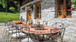 Un bâtiment en pierre avec une façade en bois, une table ronde entourée de chaises et une fenêtre ornée de fleurs.