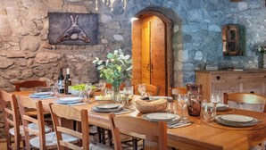 Une salle à manger rustique avec un mur en pierre, des poutres en bois au plafond et une table à manger en bois, dressée pour six personnes.