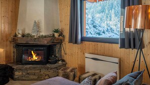 L’intérieur d’un chalet chaleureux, avec une cheminée en pierre, des murs en bois, une fenêtre donnant sur un paysage enneigé et une lampe moderne.