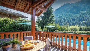 Une terrasse en bois avec une table dressée pour le repas, offrant une vue sur une piscine et des montagnes boisées.