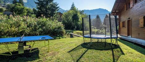 En baghave med trampolin, bordtennisbord og et træhus med udsigt til et bjerg.