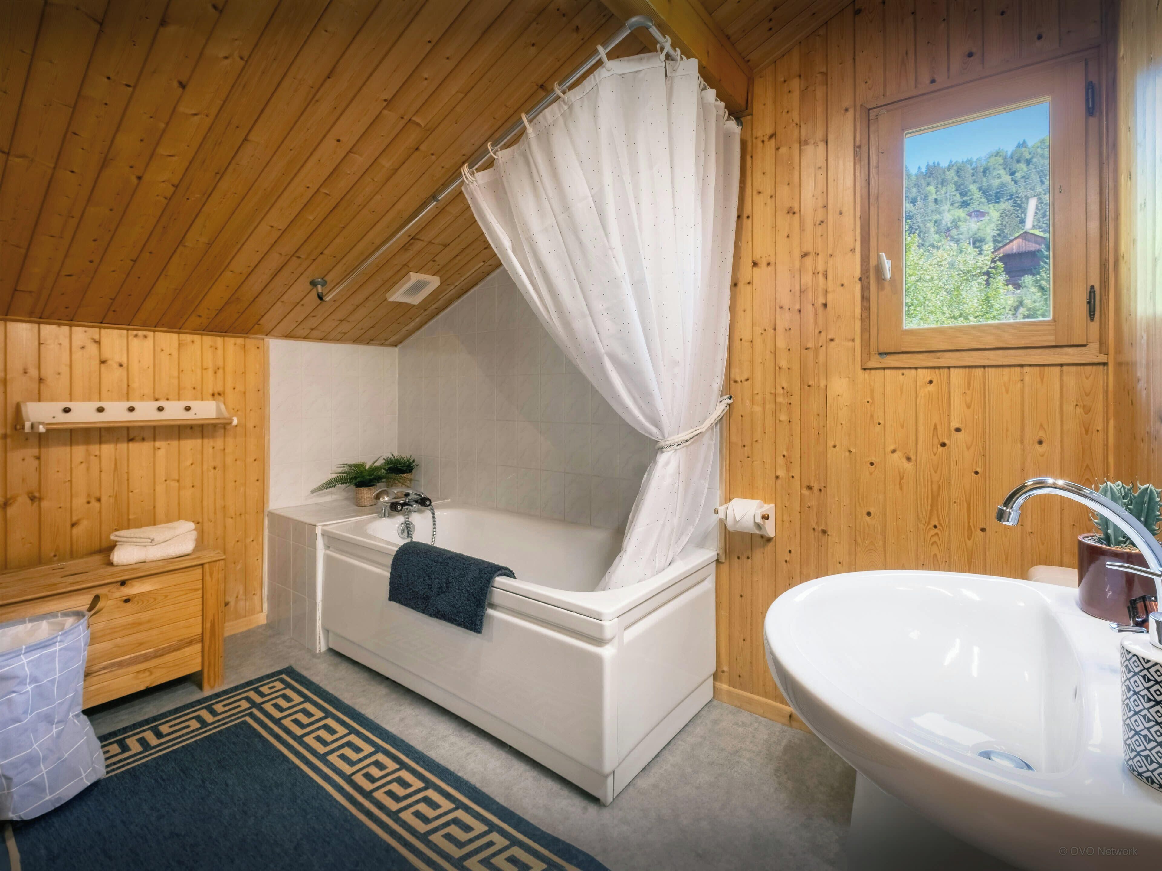 A wooden cabin bathroom with a bathtub, a sink, and a window with a view of trees.
