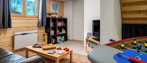 A cozy living room with a foosball table, a television, a bookshelf, and a window with curtains.