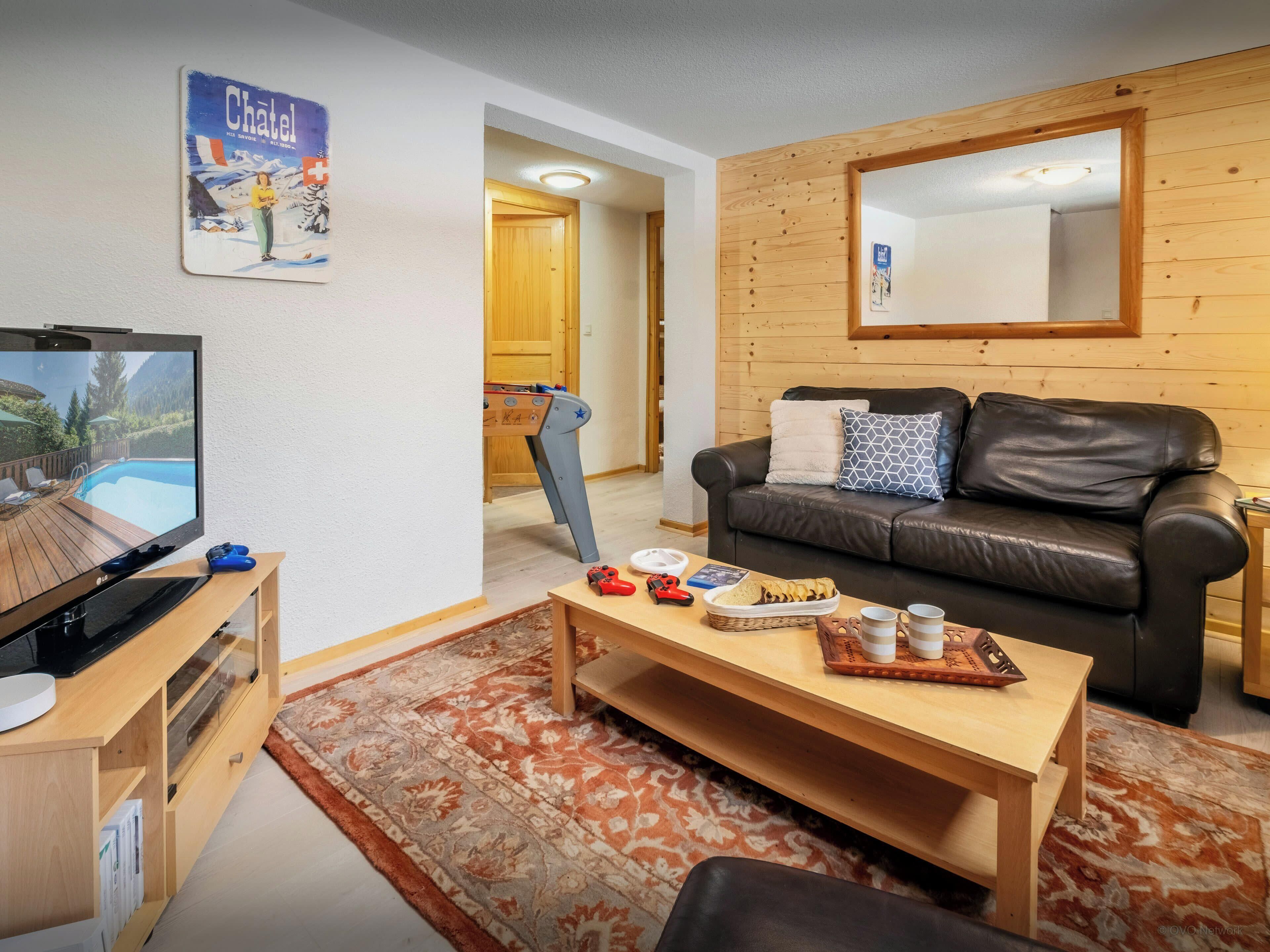A cozy living room with a flat-screen TV, a wooden coffee table, a leather sofa, and a futsal table.