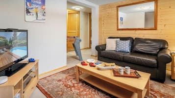 A cozy living room with a flat-screen TV, a wooden coffee table, a leather sofa, and a futsal table.