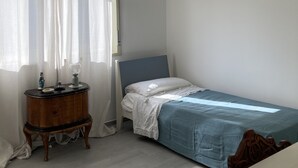 Un dormitorio con una cama individual, un aparador, una araña y cortinas traslúcidas.