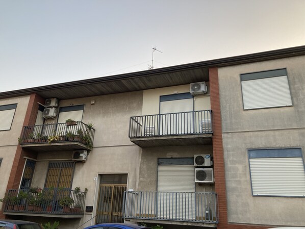 A multi-story building with balconies, air conditioning units, and a closed shutter door.