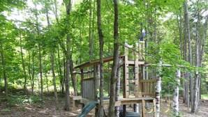 A wooden play structure with a slide in a forested area.