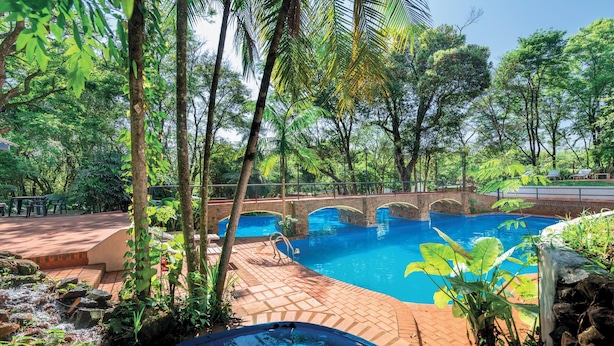 A swimming pool with a bridge, surrounded by lush greenery and a stone pathway. - El Leñador (Puerto Iguazú)