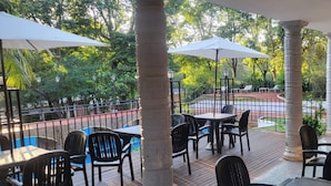 An outdoor patio area with tables and chairs, surrounded by trees and a pool. - El Leñador (Puerto Iguazú)