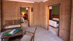 A room with a brick wall, a wooden bench, a bed, and a table with a tray of cups and saucers. - El Leñador (Puerto Iguazú)