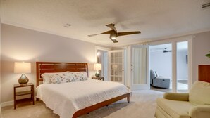 A bedroom with a bed, bedside tables, a ceiling fan, a chair, and a door leading to a balcony. - Poolside Oasis Near Medical Center & NRG Stadium! (Houston)