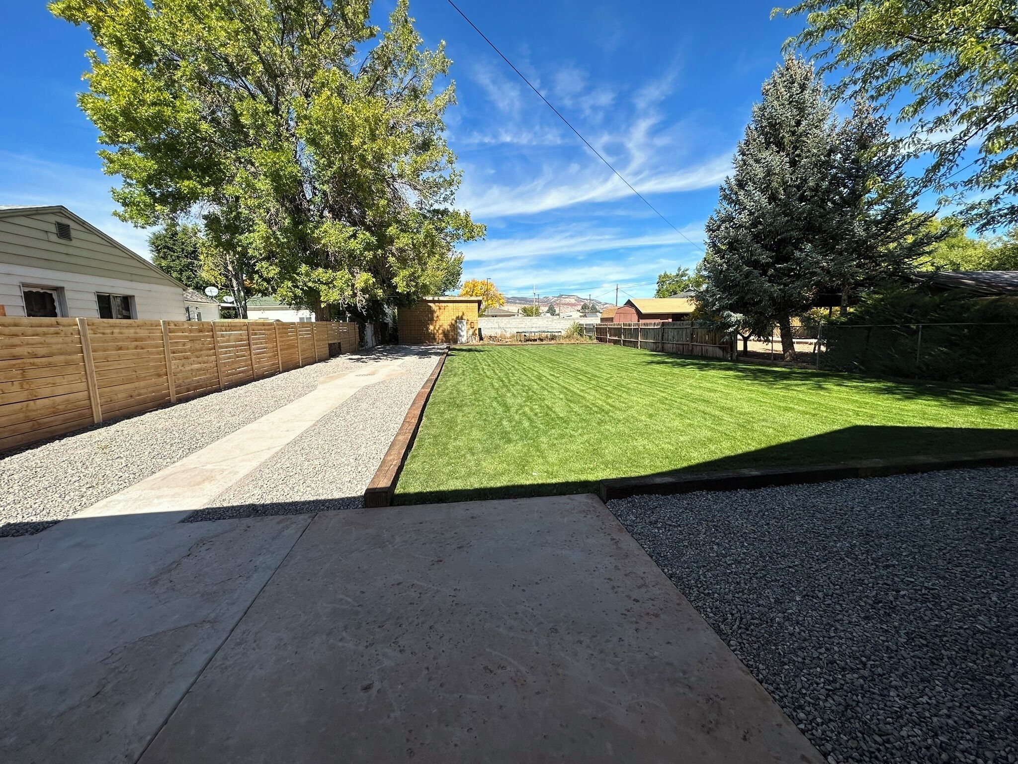 A backyard with a lawn, gravel path, wooden fence, and a house in the background.