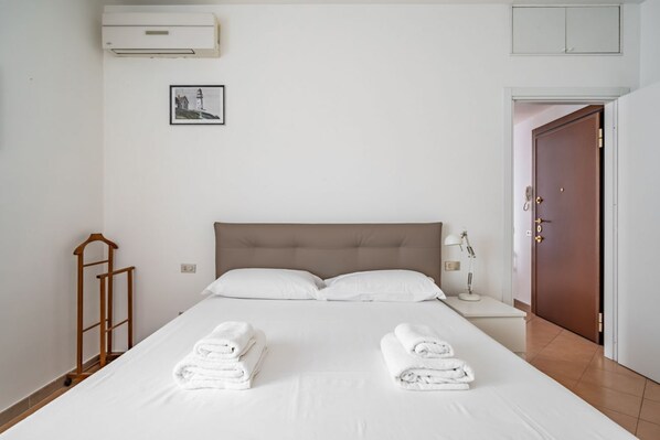 A neatly made bed with two folded towels, a bedside lamp, and a framed picture on the wall.