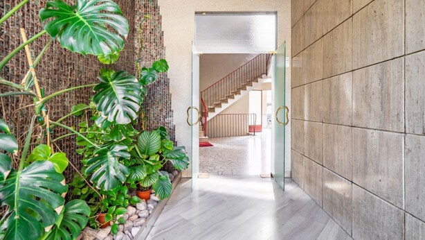 Un couloir avec un escalier, une porte en verre et un mur orné d’un motif texturé.