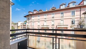Un balcon donnant sur un immeuble rose, doté de balcons et de fenêtres, d’une rambarde en métal et d’un radiateur.